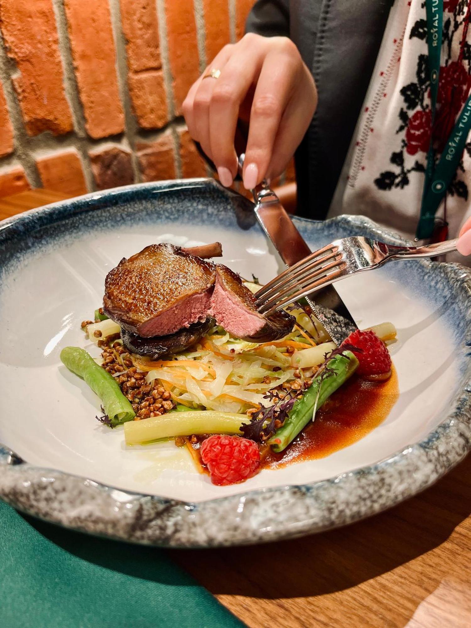 Aparthotel Royal Tulip Warsaw Centre Esterno foto The photo shows a beautifully plated dish featuring a slice of meat, likely a duck or similar, that is perfectly cooked with a reddish center. The meat is garnished and served alongside a mix of vegetables, which include green asparagus and possibly 